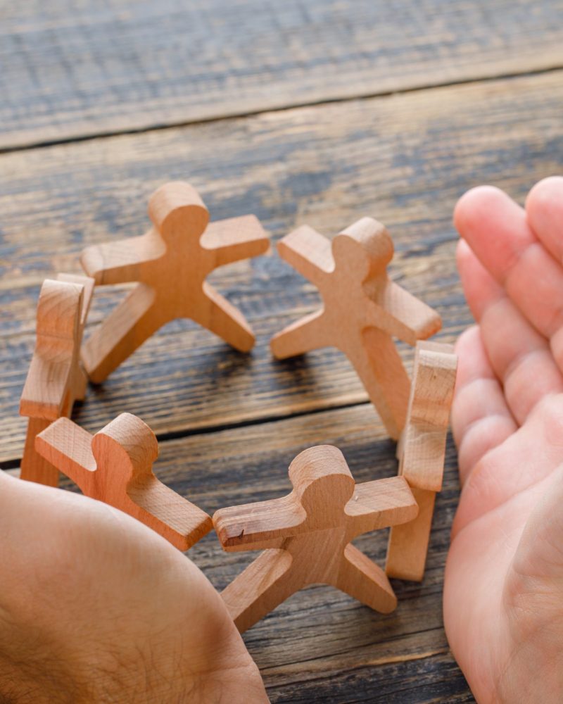 Business success concept on wooden background high angle view. hands protecting wooden figures of people.